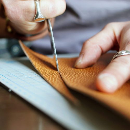Magnetbags Leather Workshop Men's hands close-up cut a piece of genuine leather to make a wallet.